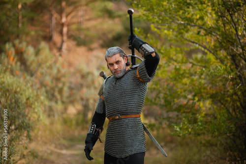 An aged male warrior in chain mail with gray hair and a scar on his face. Knight in armor holds a two-handed sword.