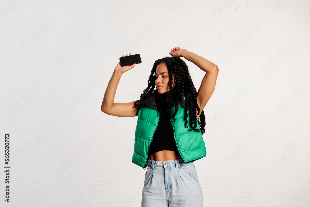A young woman dancing as her arms raised while holding her cell phone in a studio shot A young woman dancing as her arms raised while holding her cell phone in a studio shot