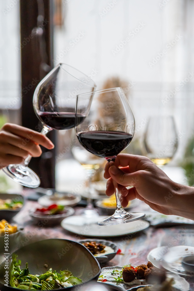 Obraz premium Close up of hands young couple clinking with glasses of red wine at restaurant
