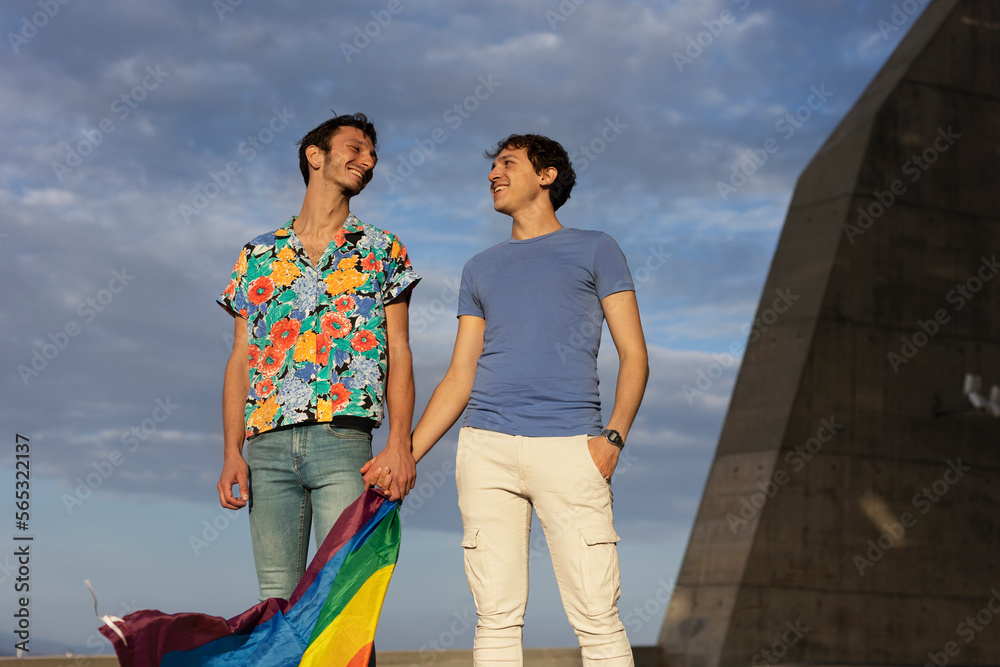 Happy young couple with rainbow flag. Two men enjoy outside..