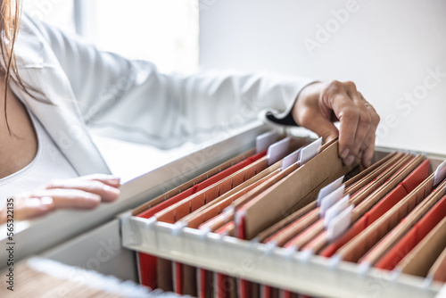 The clerk is leafing through stored folders, looking for a file or document. Concept of data storage, filing cabinet and business administration. photo