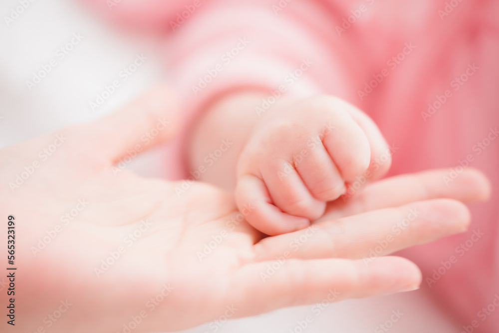 Close up mother holding hands newborn girl in a room. Adorable infant rests on white bedsheets, staring at camera looking peaceful. Infancy, healthcare and paediatrics, babyhood concept. Close up mother holding hands newborn girl in a room. Adorable infant rests on white bedsheets, staring at camera looking peaceful. Infancy, healthcare and paediatrics, babyhood concept.