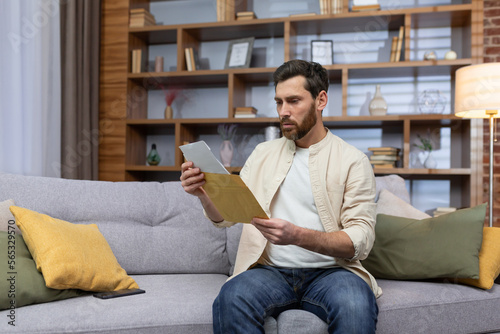Upset young man sitting on sofa at home, received a letter, reads bad news. Divorce documents, financial debt, rent, credit, Upset young man sitting on sofa at home, received a letter, reads bad news © Liubomir