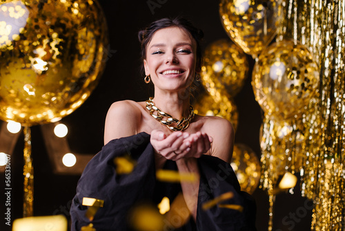 Happy woman throws confetti and celebrates the holiday. Beautiful smile and enjoyment. Party birthday. New Year's Eve. Dance at the night disco. Congratulations on the holiday. Stylish sexy girl joy