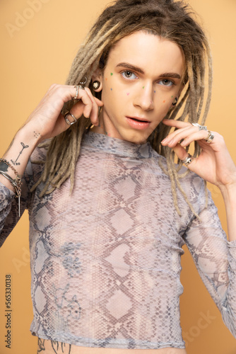 Portrait of tattooed queer person with dreadlocks looking at camera isolated on yellow.