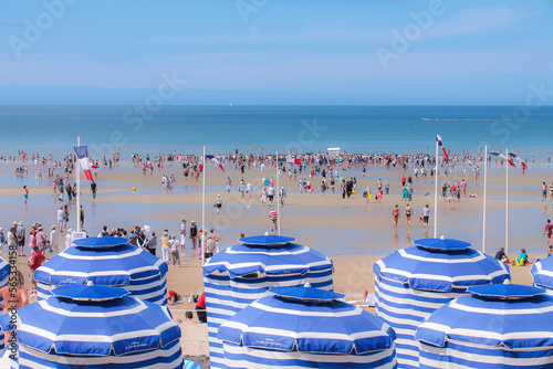 Fotografie A normandy beach with rows of white and blue parasols
at low tide and a crowd of