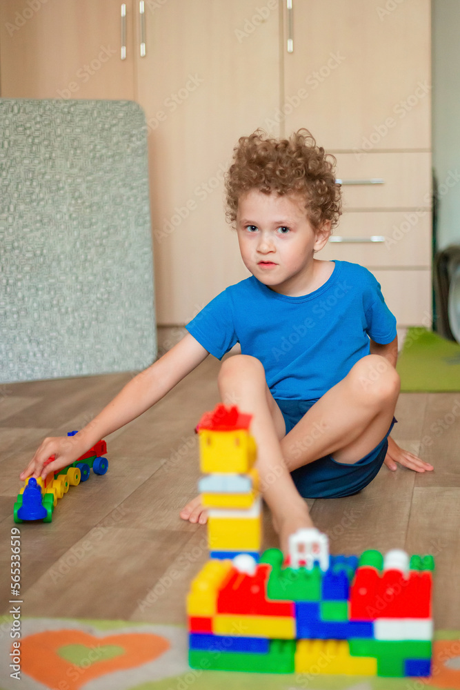 Little curly boy plays with toys. The child builds a house from a colored constructor. Little curly boy plays with toys. The child builds a house from a colored constructor.