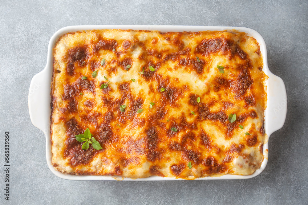 Portion of ground beef lasagna topped with melted cheese and garnished with fresh parsley served on a plate in close view for a menu