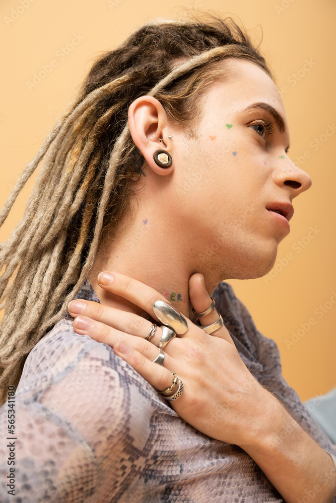 Tattooed nonbinary person with dreadlocks and rings posing isolated on yellow.