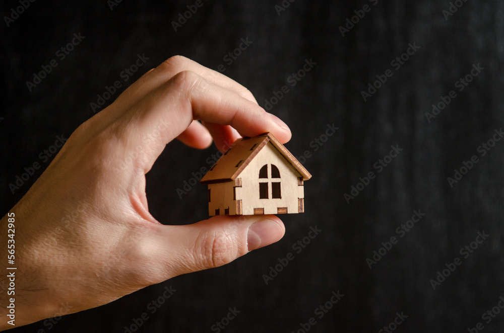 One small wooden house on a man hand on black background, the concept of family happiness, buying a house One small wooden house on a man hand on black background, the concept of family happiness, buying a house