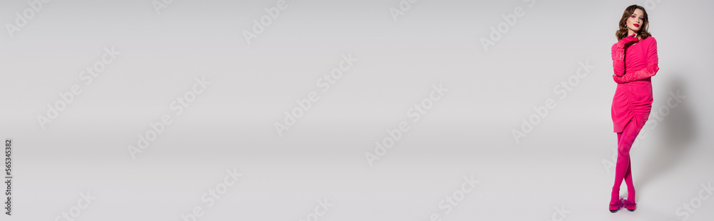 full length of young woman in magenta color dress and shoes posing on grey background, banner.