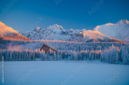 The serenity of Strbske Pleso lake amidst the High Tatras mountains, as the sun rises on a chilly winter morning