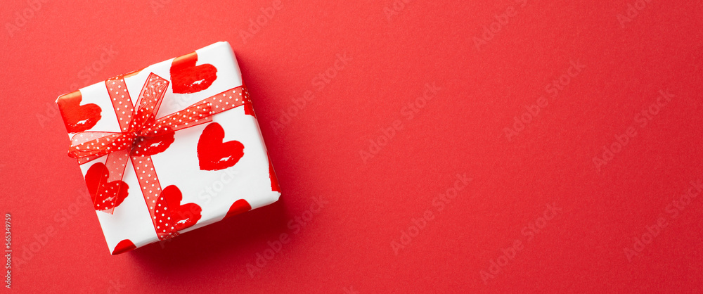 Valentine's Day concept. Top view photo of white giftbox in wrapping paper with heart pattern and ribbon bow on isolated red background with copyspace