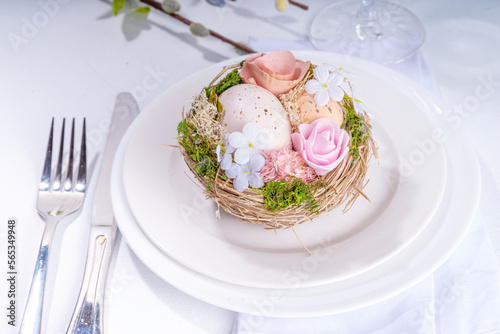 Easter table setting. Festive spring holiday cutlery set, with plate, wine glass, knife, fork, with Easter decor egg nest, willow flower branches, white sunny table background copy space top view