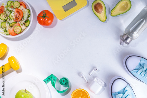 Spring slim and fitness, active living concept. Small yellow dumbbells, bottle of water, sports shoes, scales, salad, fresh vegetables and fruits on a light white background, top view copy space