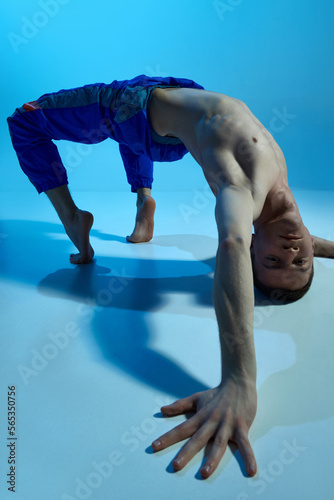 Contemporary dance style. Young artistic man dancing contemp, experimental dance over blue studio background. Flexible artist. Concept of art, body aesthetics, motion, action, inspiration.