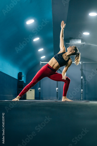 Young fit woman in sportswear doing yoga at gym in extended side angle pose.