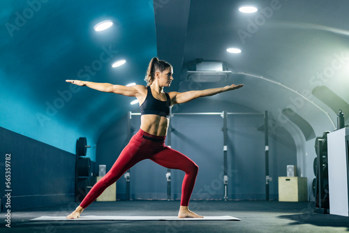 Young fit woman in sportswear doing yoga at gym in warrior II pose.