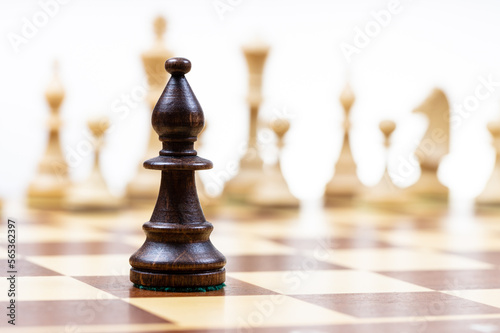 Canvas Print black bishop against white chess figures in background on wooden chessboard clos
