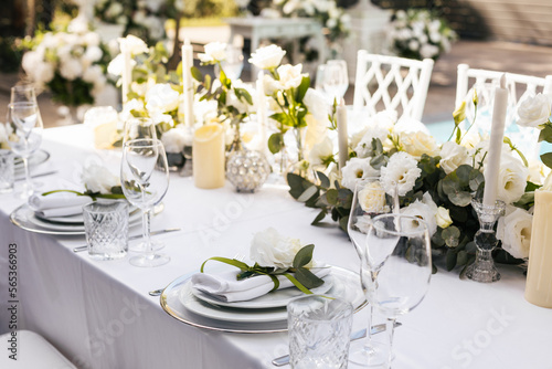 Wedding decorations. Served wedding table with decorative fresh white flowers and candles. Celebration details. flower composition roses plates and candles in candlesticks