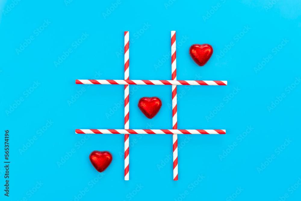 Heart shaped chocolates in red foil on blue background, tic-tac-toe game, creative concept, flat lay. Heart shaped chocolates in red foil on blue background, tic-tac-toe game, creative concept, flat lay.