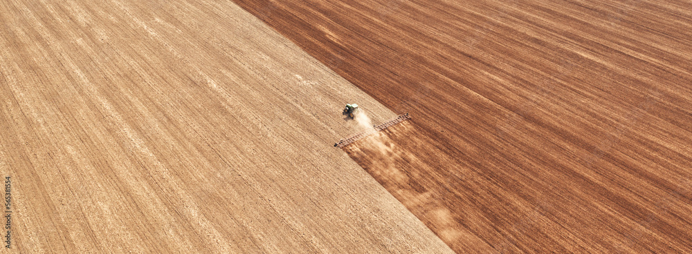 Fototapeta premium A tractor in the field cultivates the soil before the start of the sowing campaign. Drone view.