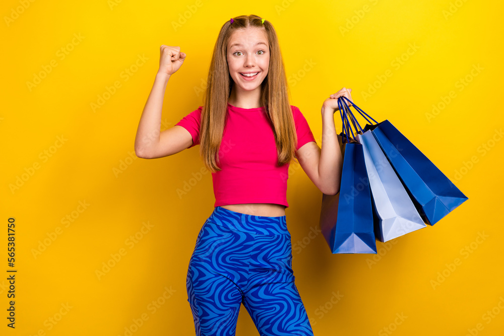Photo of young fashionista retro outfit teenage girl wear blue sport trousers fist up hold much bags shopping isolated on yellow color background Photo of young fashionista retro outfit teenage girl wear blue sport trousers fist up hold much bags shopping isolated on yellow color background