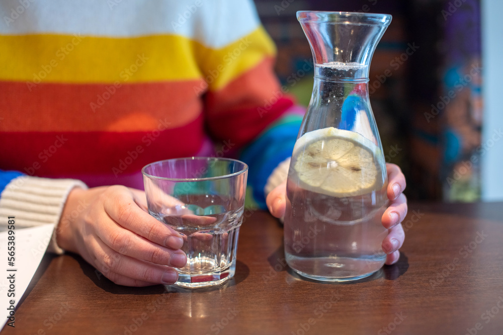 Women's hands hold a carafe of water and lemon next to a glass glass. Sweater with LGBT flag Women's hands hold a carafe of water and lemon next to a glass glass. Sweater with LGBT flag