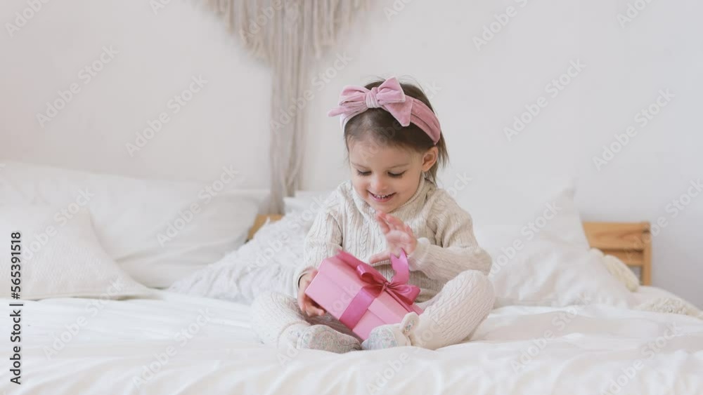 Cute funny baby girl on a crib with a gift in a bright room. The child is having fun at home. Wide angle horizontal wallpaper or web banner. Cute funny baby girl on a crib with a gift in a bright room. The child is having fun at home. Wide angle horizontal wallpaper or web banner.