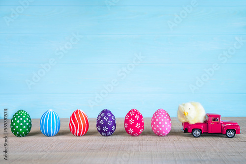 Fototapete Easter composition with yellow fluffy fledgling chicken at pink car and colored easter eggs against the blue wooden background