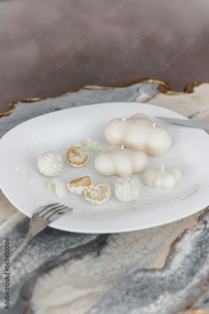 Shaped white candles handmade in a modern style, beautifully shaped on a white plate. serving plate with rafaelo candy. 