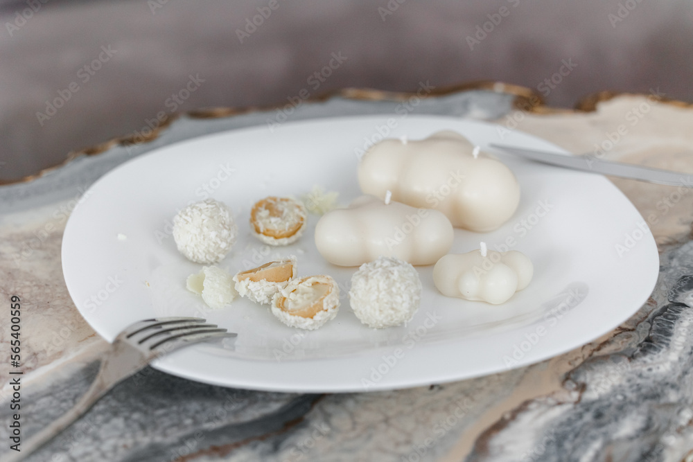 Shaped white candles handmade in a modern style, beautifully shaped on a white plate. serving plate with rafaelo candy. Shaped white candles handmade in a modern style, beautifully shaped on a white plate. serving plate with rafaelo candy.