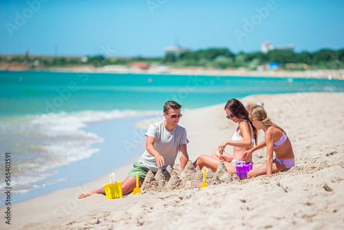 Parents and little daughter enjoying time on the beach. Family making sand castle together on the seashore