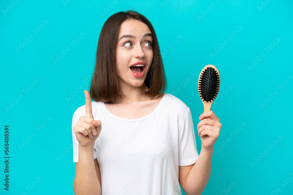 Young ukrainian woman with hair comb isolated on blue background intending to realizes the solution while lifting a finger up Young ukrainian woman with hair comb isolated on blue background intending to realizes the solution while lifting a finger up