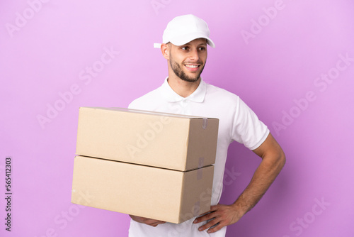 Delivery caucasian man isolated on purple background posing with arms at hip and smiling