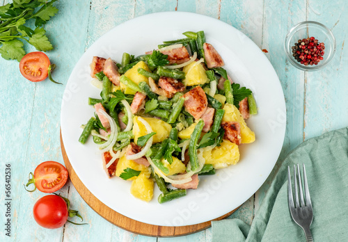 Liege salad is a Belgian dish from the Liege region with potatoes, bacon and green beans, white plate, wooden background, top view.