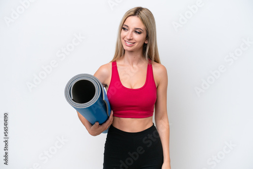Young sport blonde woman going to yoga classes while holding a mat isolated on white background looking to the side and smiling © luismolinero