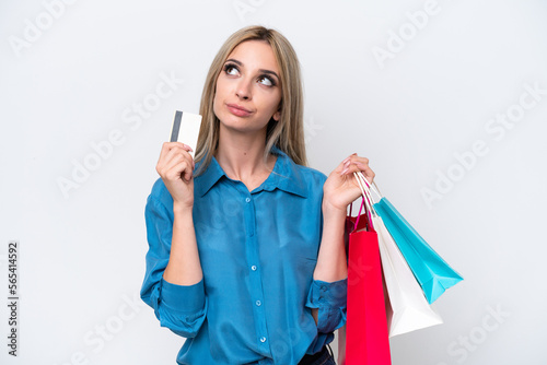 Pretty blonde woman isolated on white background holding shopping bags and a credit card and thinking