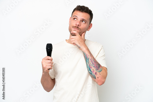 Young caucasian singer man picking up a microphone isolated on white background and looking up