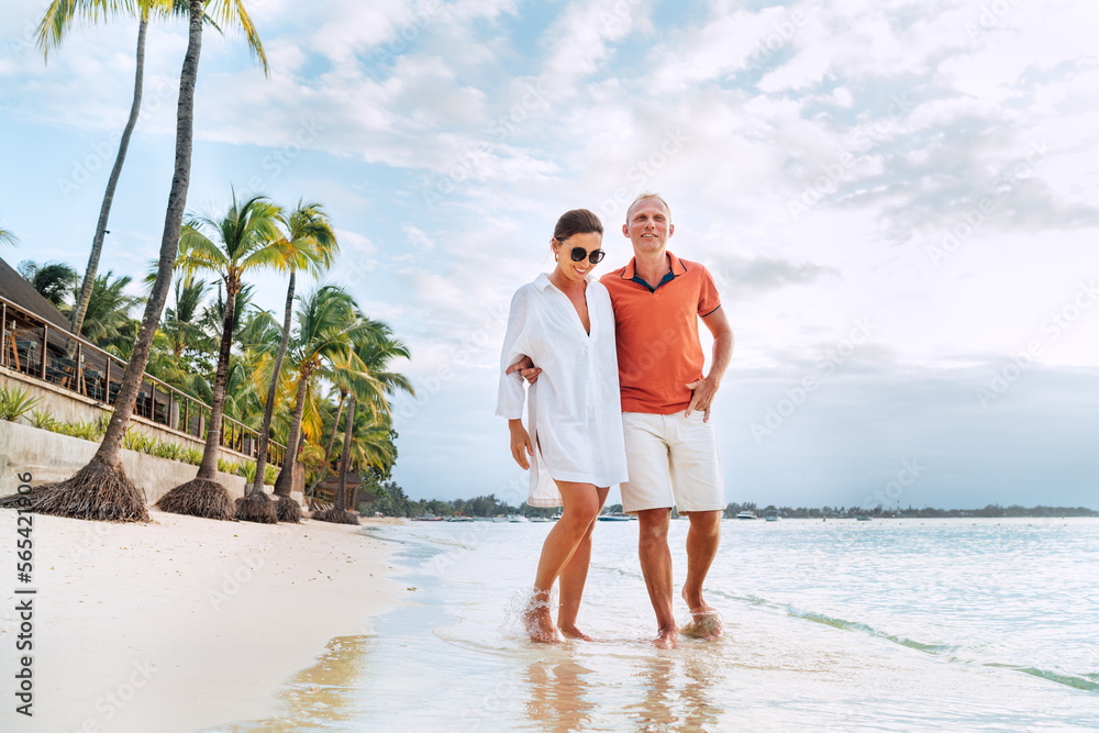 Couple in love hugging while walking on a sandy exotic beach. They have an evening walk by Trou-aux-Biches seashore on Mauritius island. People relationship and tropic honeymoon vacations concept
