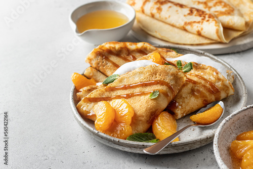 Crepes with fresh mandarin, caramel, cream in the filling and mint leaves on white textured background. Maslenitsa or Pancake week traditional concept, text space