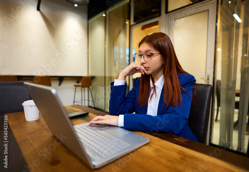 portrait young latin woman formally dressed with a laptop pensive looking at the screen in an office