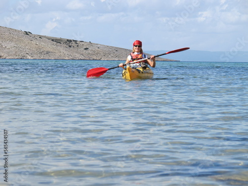A woman paddles a yellow kayak on a sunny day in the Mediterranean Sea in Croatia. Beautiful views of the rocky coast. Active lifestyle.  © LINDA