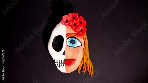 Stop motion claymotion animation. The plasticine head of a woman is divided into skull bones, and on the other side flowery hair with a red crown. A girl with a blue eye blinks. Halloween photo