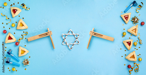 Purim celebration jewish carnival holiday concept. Tasty hamantaschen cookies, Carnival mask, noisemaker, sweet candies and party decor on blue background. Top view, flat lay, copy space.