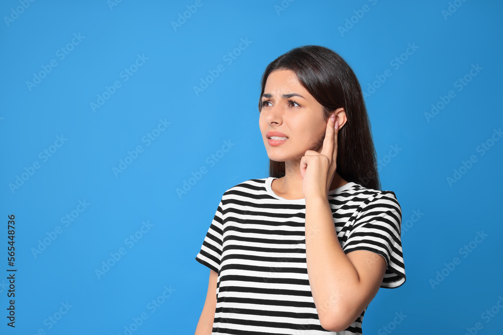 Young woman suffering from ear pain on light blue background. Space for text Young woman suffering from ear pain on light blue background. Space for text