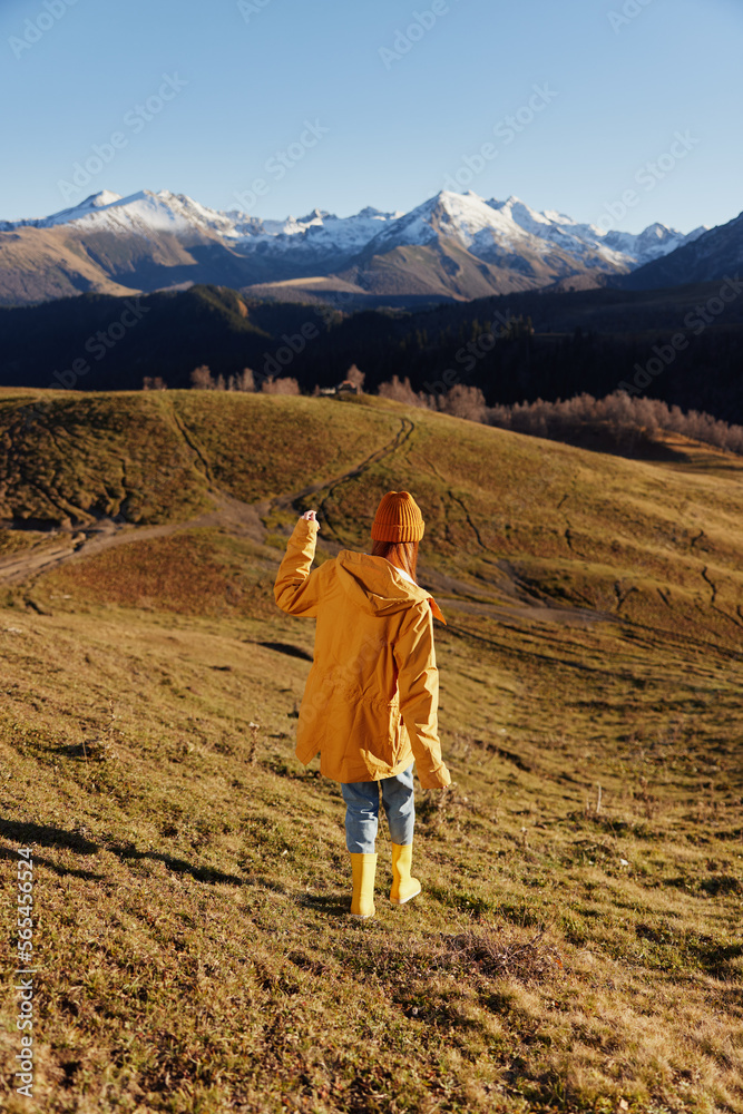 Woman's back full-length running up the hill and looking at the mountains in yellow raincoat and jeans in the autumn happy trip in the sunset sunset camping, freedom lifestyle 