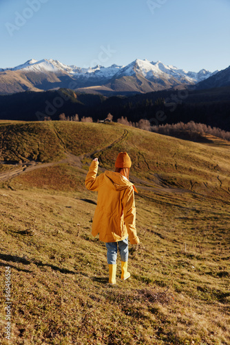 Woman's back full-length running up the hill and looking at the mountains in yellow raincoat and jeans in the autumn happy trip in the sunset sunset camping, freedom lifestyle  © SHOTPRIME STUDIO