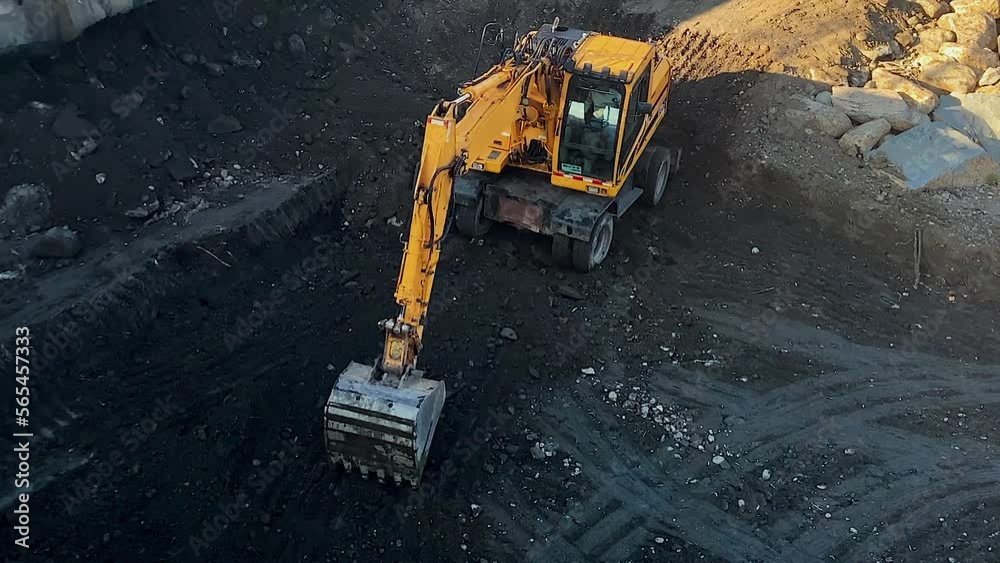 Long shot: the yellow excavator digs black ground with a bucket