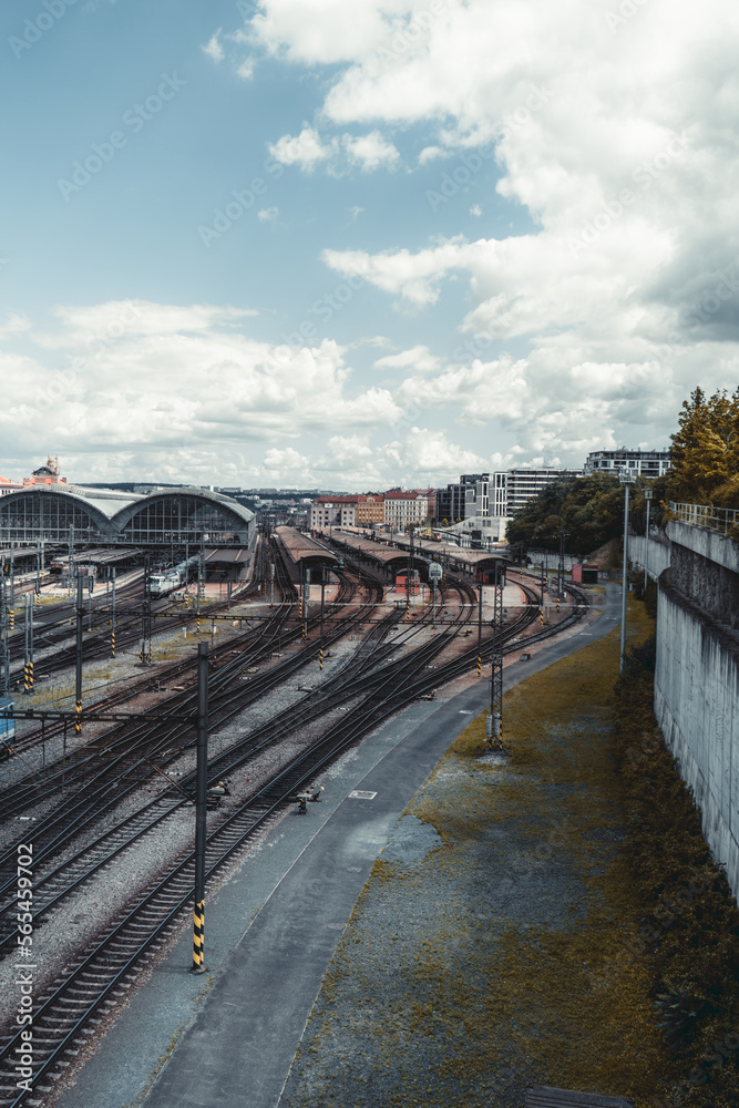 A vertical shot of a contemporary railroad terminal depot station with plenty of railway junctions and branches, outdoor and indoor platforms, trains, and locomotives on a cloudy day, Prague